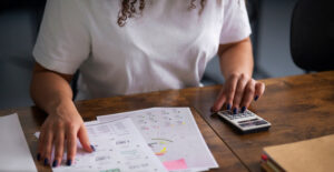 Empresária calculando fluxo de caixa e impostos com planilhas e calculadora na mesa