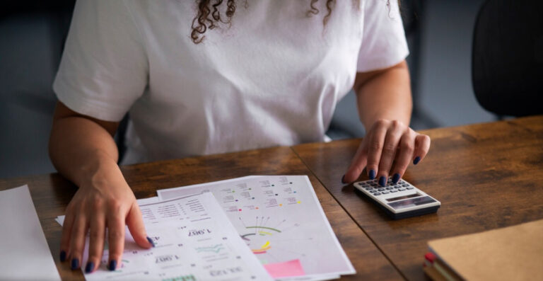 Empresária calculando fluxo de caixa e impostos com planilhas e calculadora na mesa