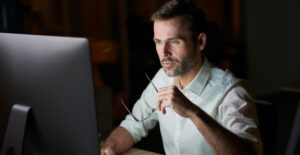 Homem analisando finanças no computador, refletindo sobre os riscos de misturar contas pessoais e da empresa