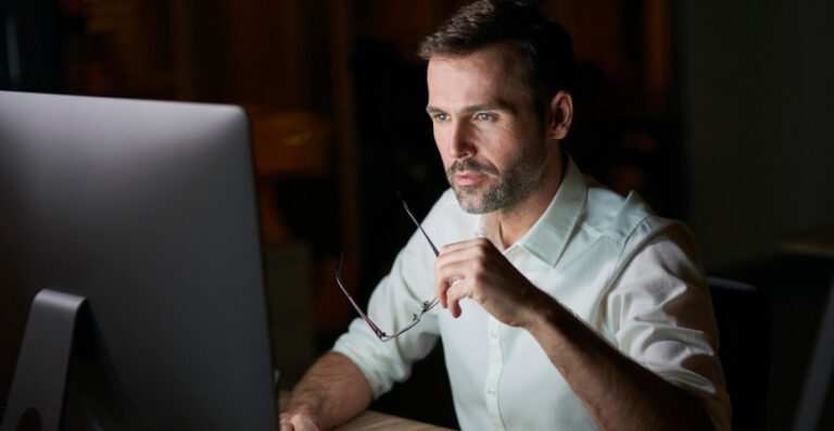 Homem analisando finanças no computador, refletindo sobre os riscos de misturar contas pessoais e da empresa